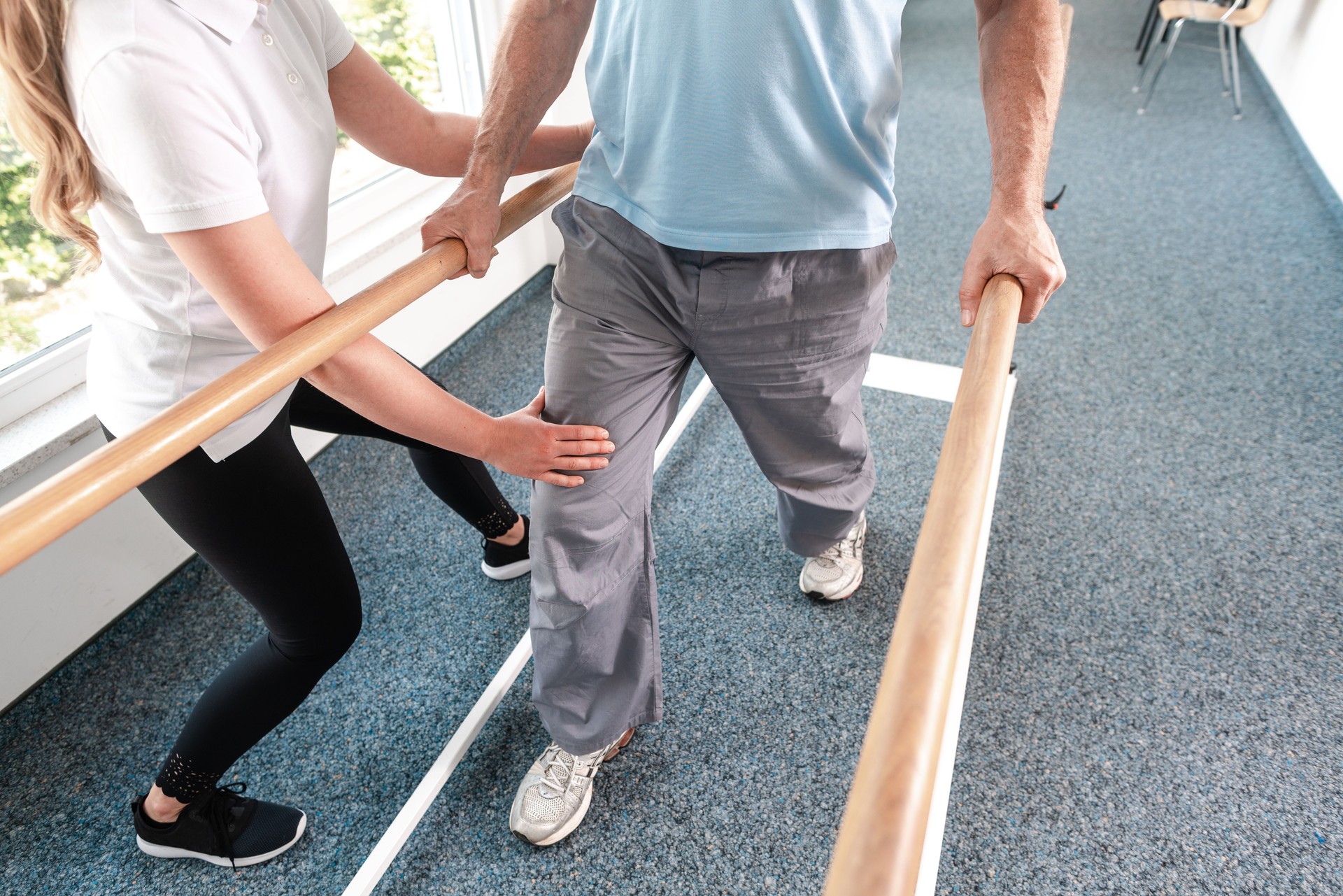 Physiotherapist helping senior man in rehabilitation walking on the bars