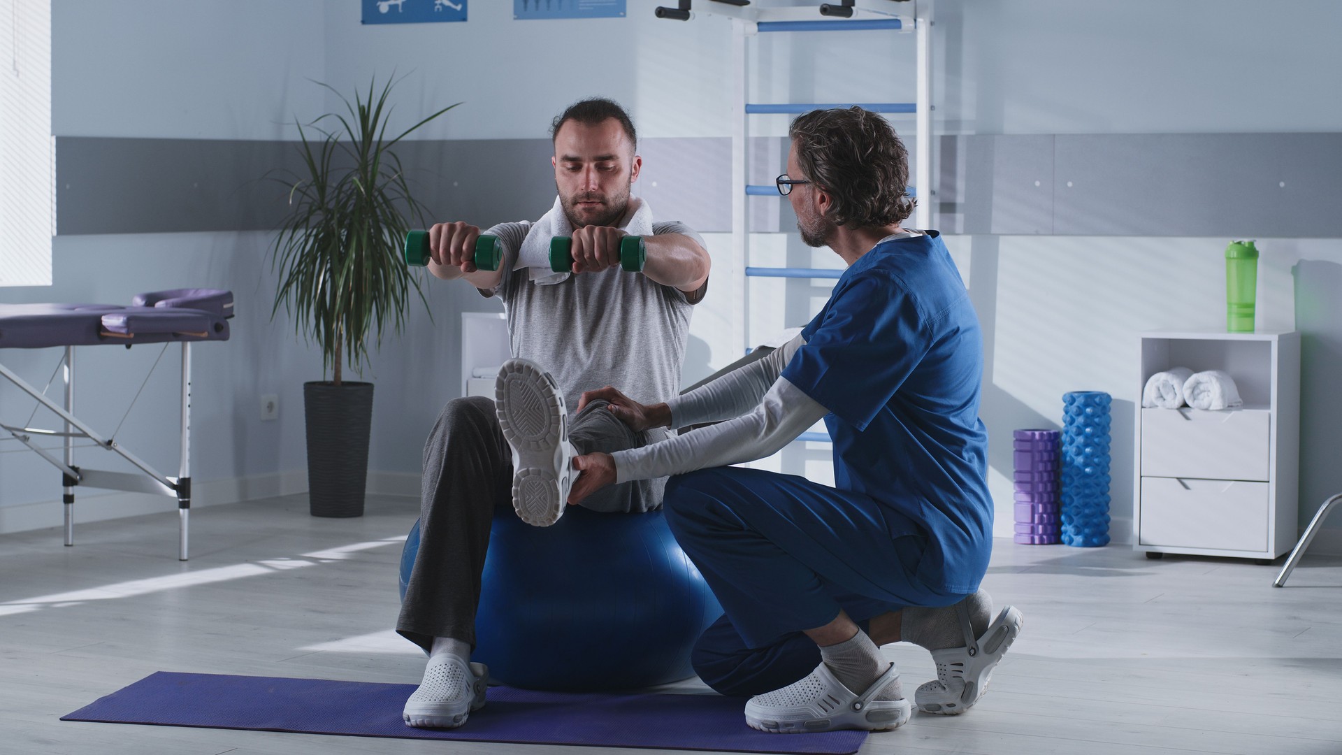 Mature therapist supporting male patient on fit ball