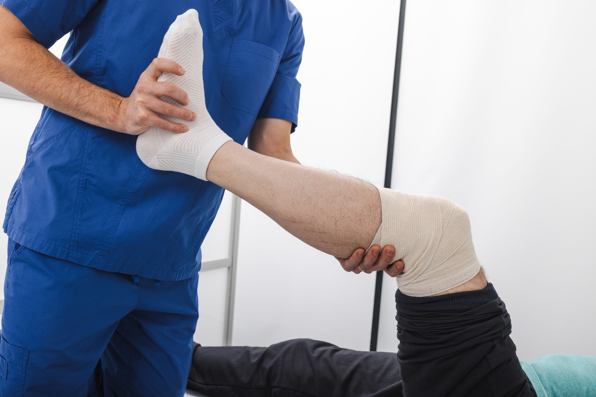 Physical therapist assists patient with leg rehabilitation in a clinical setting. Healthcare professional gently adjusts a patient's bandaged leg to aid in recovery