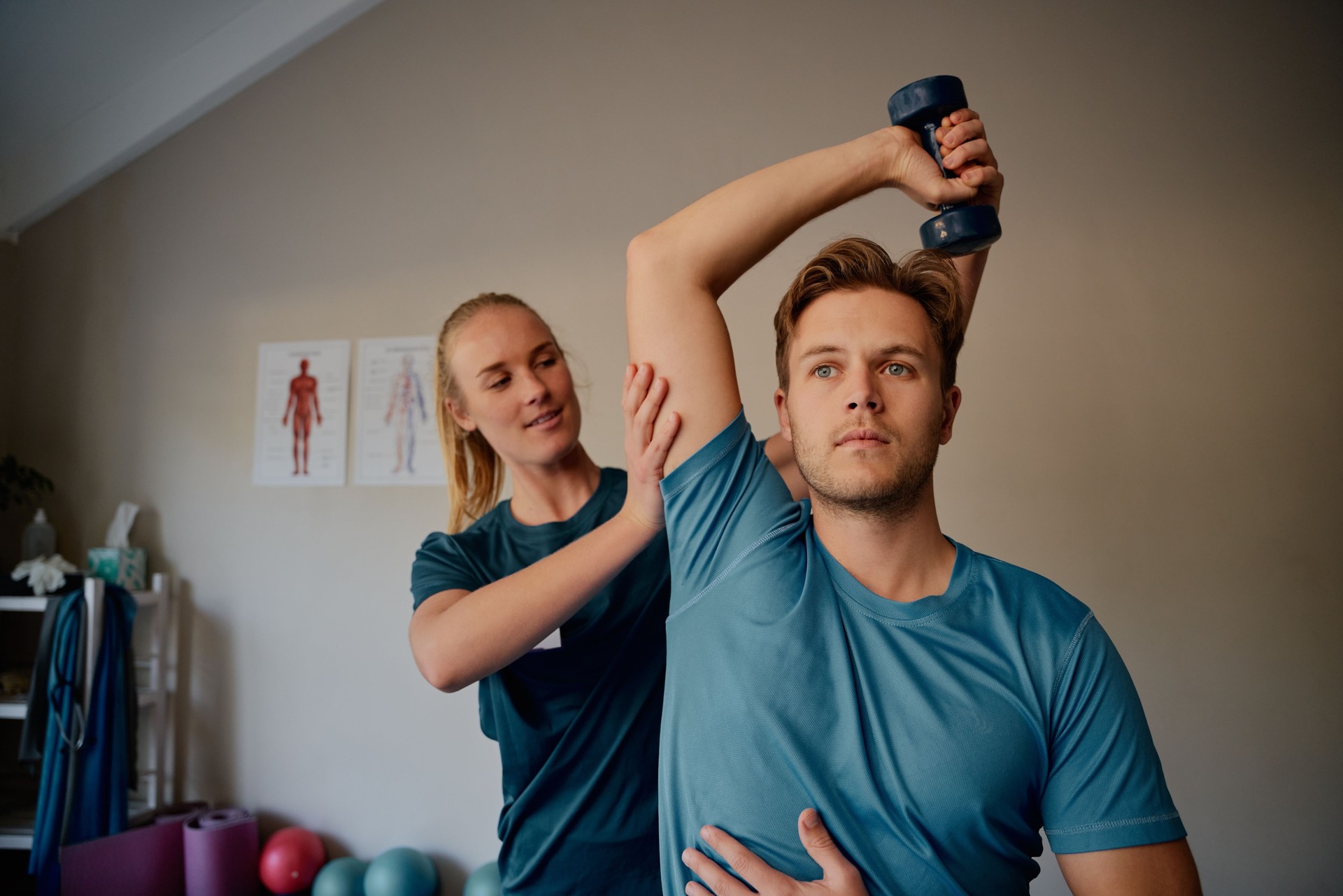 Young female physiotherapist helping patient to raise dumbbells in rehabilitation centre