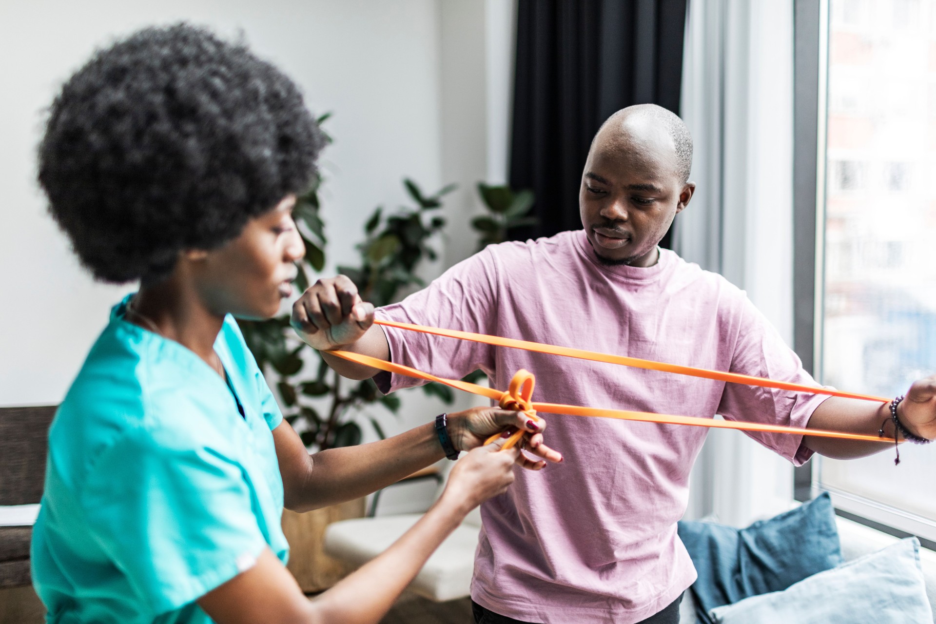 Young black physiotherapist working with patient at home doing exercises with exercise band