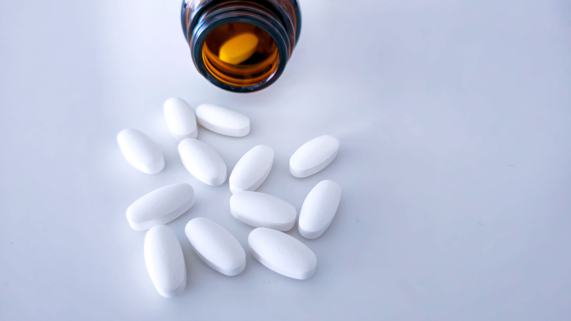 White pills spill out of the bottle onto the table
